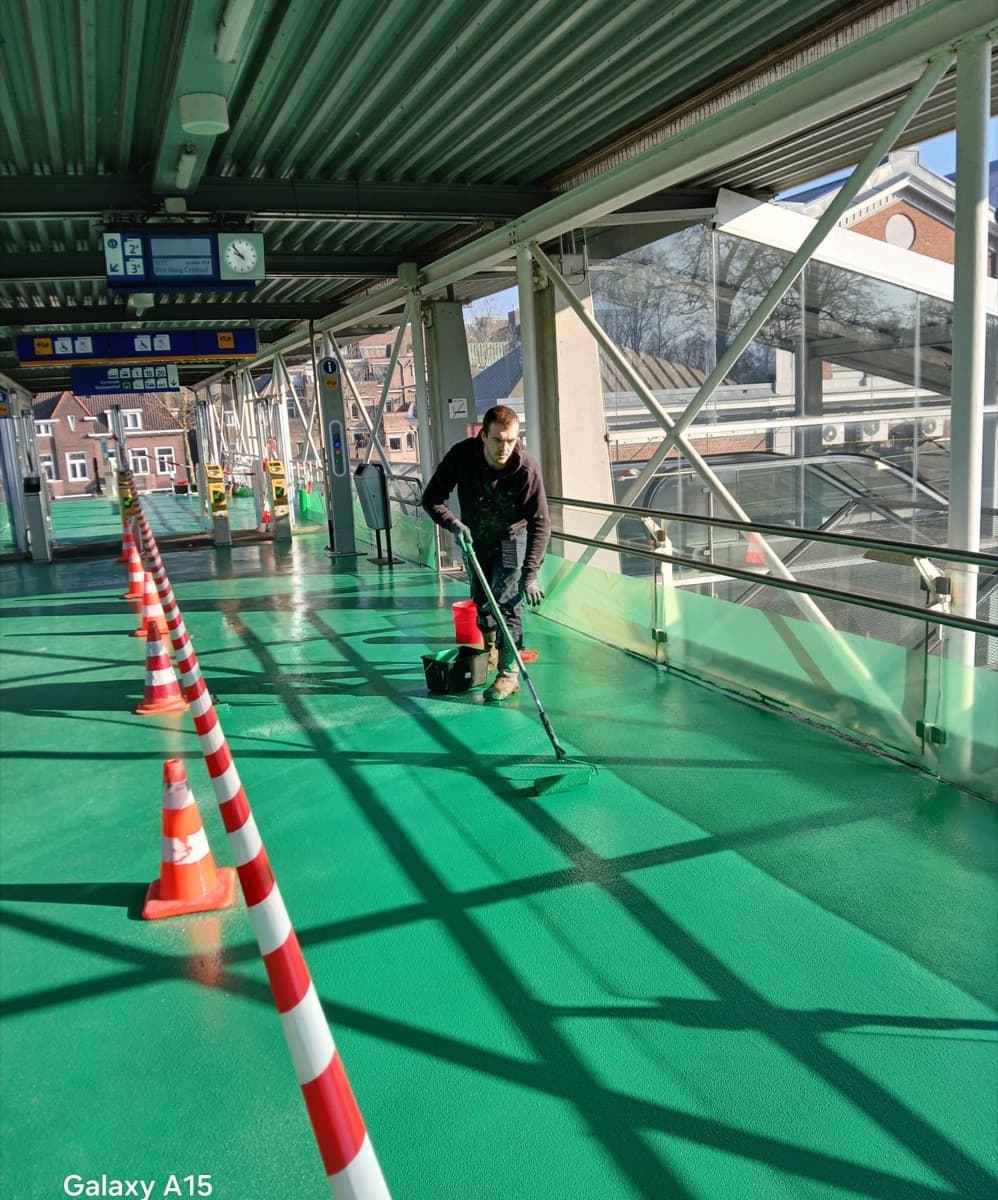 Een vakman van Kitfix brengt antislipcoating aan op de loopbrug van station Dordrecht
